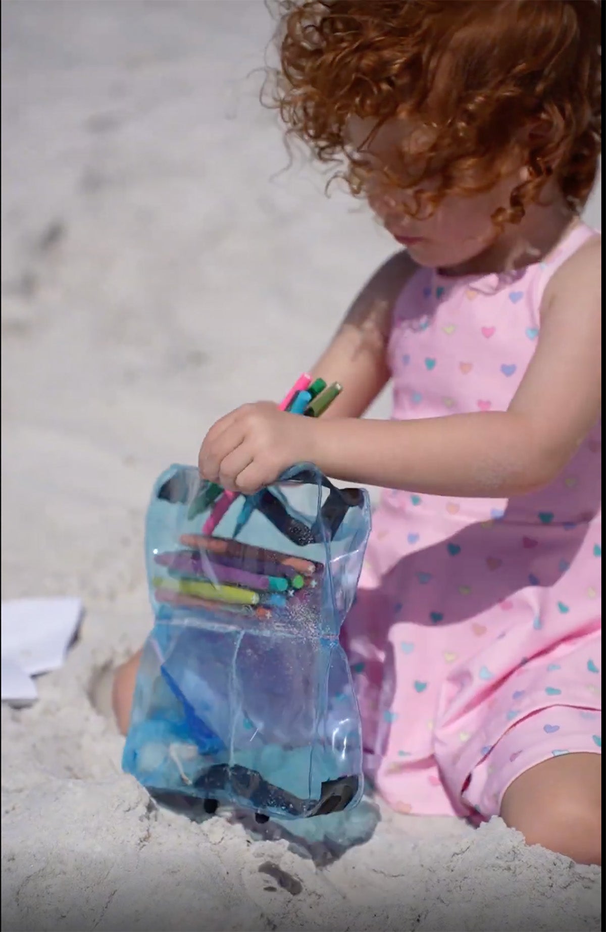Toddler at the beach with a Blue DivideNPac organizer filled with colorful crayons on the sand.