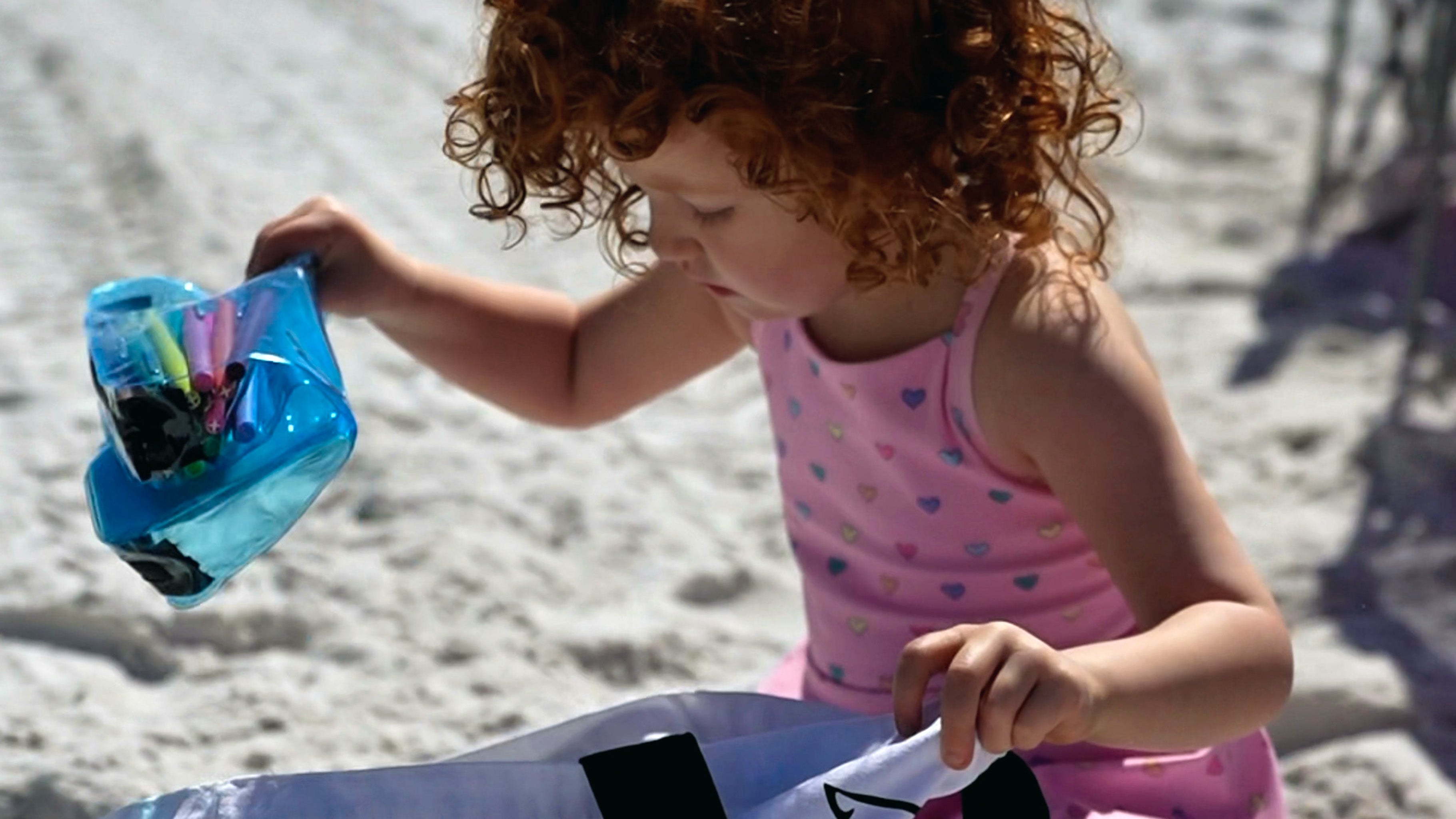 Toddler at the beach with a Blue DivideNPac organizer filled with art supplies on the sand.