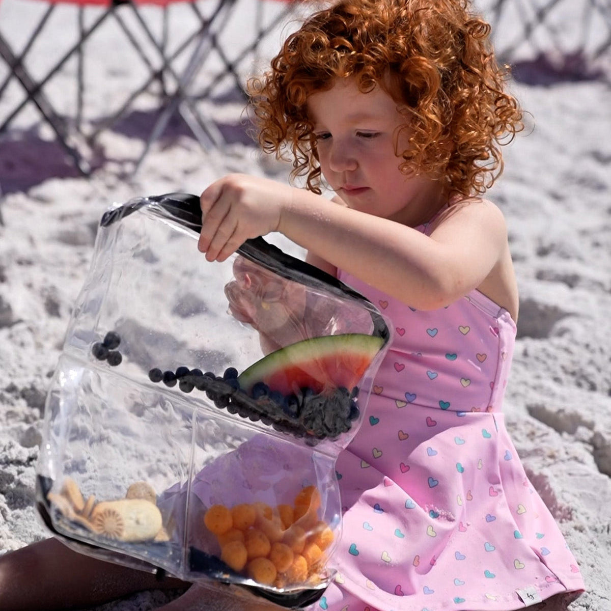 Toddler at the beach with a DivideNPac food-grade organizer filled with fresh blueberries, watermelon, oranges, and cheese.