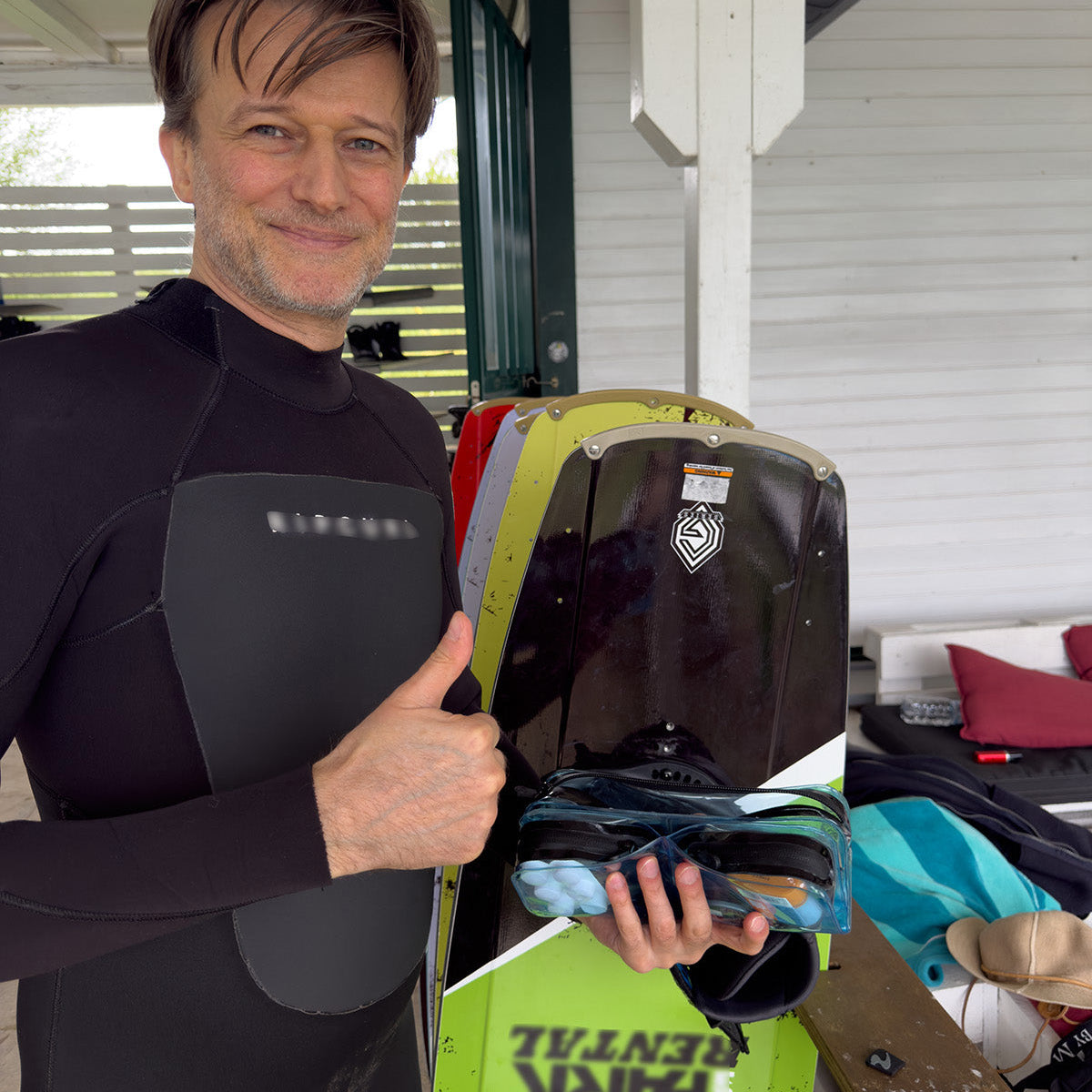 Customer in a wetsuit holding water skis and a DivideNPac organizer with his gear, giving a thumbs up.